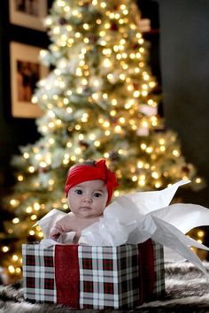 a baby sitting in a gift box with a christmas tree behind it