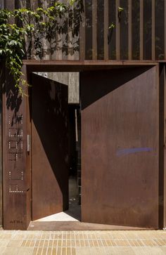 an open wooden door on the side of a building next to a brick sidewalk and tree