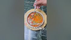 a person holding a spoon over a bowl of food with the words instant dal tadka on it