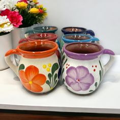 four flowered mugs are lined up on a table with flowers in the background