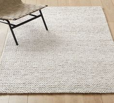 a chair sitting on top of a wooden floor next to a white rug with braided edges