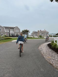 two people riding bikes on a paved road next to houses and the ocean in the background