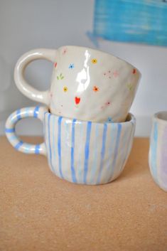 three coffee cups sitting on top of a table next to each other, one has a blue and white stripe pattern