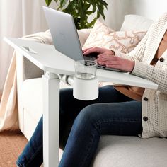 a woman sitting on a couch using a laptop computer with a coffee cup in front of her