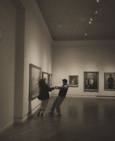 two people standing in an art gallery looking at paintings