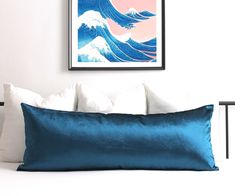 a large blue pillow sitting on top of a white bed next to a framed painting