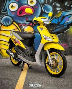 a yellow and silver scooter parked in front of a wall with graffiti on it