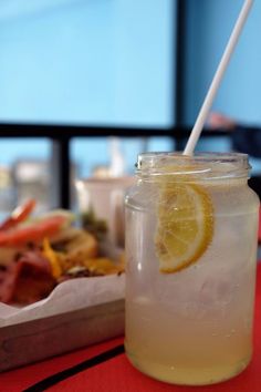 a drink with lemon and ice sits on a table next to a tray full of food