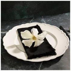 a white plate topped with a black napkin and a white flower on top of it