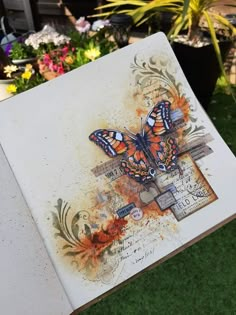 an open book with butterflies on it sitting in the grass next to potted plants