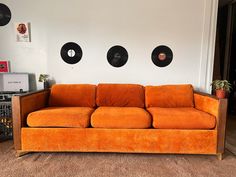 an orange couch sits in front of records on the wall behind it, and there is a record player next to it