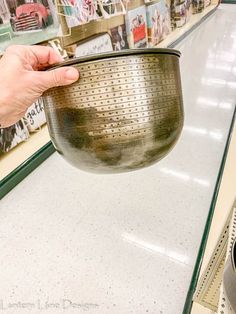 a person is holding a strainer in front of a store display case with pictures on the wall