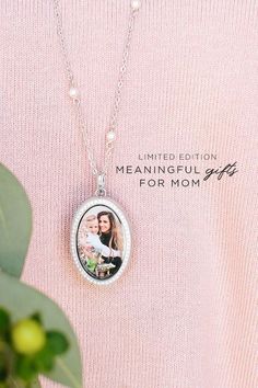 a woman wearing a pink sweater and necklace with a photo on it, next to a plant