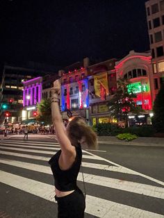 a woman is holding up her cell phone in the middle of the street at night