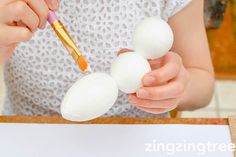 a child is painting three white eggs with a brush