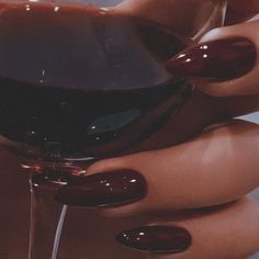 a woman's hand holding a glass of wine with red nail polish on it