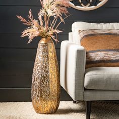 a vase with dried flowers in it next to a couch