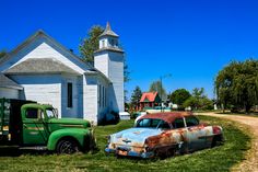 two old cars parked in front of a white church with a steeple on top