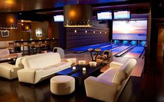 a bowling alley with couches, tables and chairs around it in front of a flat screen tv