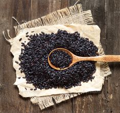 a wooden spoon filled with black rice on top of a table