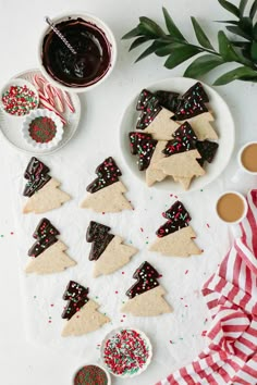 cookies decorated with christmas trees and sprinkles on a white surface next to cups of coffee