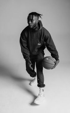 a man holding a basketball while standing in front of a white wall with his hands on the ball