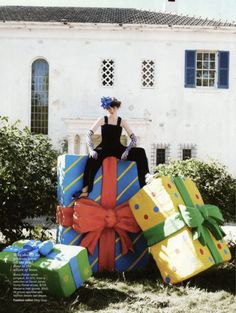 a woman sitting on top of presents in front of a white building with blue shutters