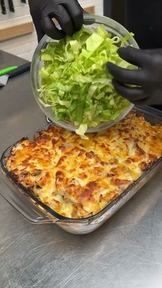 a person in black gloves puts a salad into a casserole dish