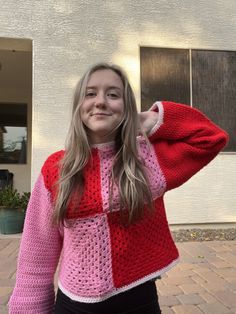 a girl in a pink and red sweater is posing for the camera with her hands on her head