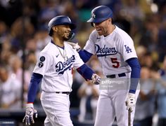 two dodgers baseball players standing next to each other on a field with fans in the background