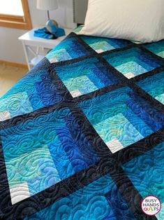 a bed with a blue and black quilt on it's headboard next to a night stand