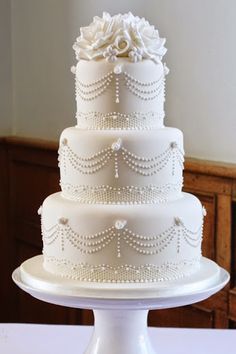 a three tiered white wedding cake with pearls and flowers on the top, sitting on a table