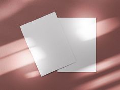 two sheets of white paper sitting on top of a pink surface with sunlight coming through the window