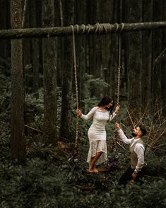 a man and woman are swinging on ropes in the middle of a forest with trees