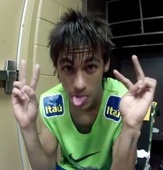 a young man making the peace sign with his fingers and wearing a green shirt in front of a mirror