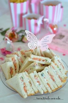 a plate full of sandwiches and cupcakes on a table with pink striped boxes in the background