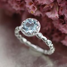 a white gold ring with an aqua blue topazte surrounded by diamonds and flowers