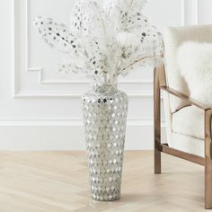 a white vase with feathers in it sitting on a wooden floor next to a chair