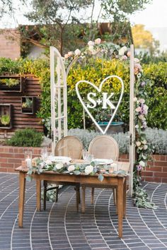 a wooden table topped with two chairs next to a heart shaped sign on top of a brick floor