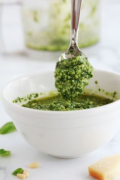 a white bowl filled with pesto sauce and a spoon full of pesto in it