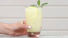 a hand holding a glass filled with liquid and a green leaf sticking out of it