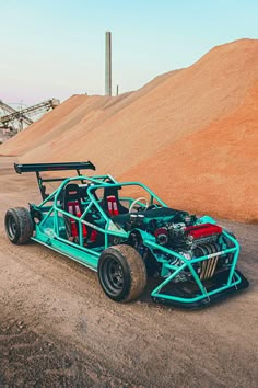 a blue race car sitting on top of a dirt road next to a pile of sand