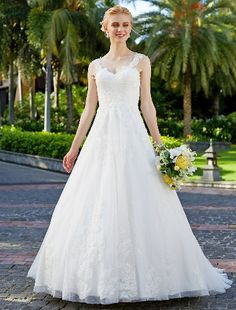 a woman in a white wedding dress standing on a brick walkway with palm trees behind her