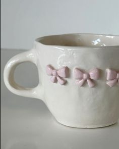 a white cup with pink bow decorations on the inside and outside, sitting on a table