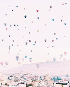 there are many hot air balloons flying in the sky above buildings and hills, with mountains in the background