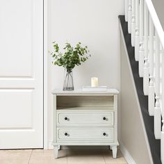 a vase with flowers sitting on top of a white dresser next to a stair case