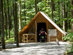 a man sitting in a tent next to a bike on a path through the woods