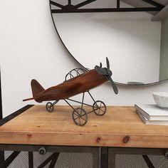 a wooden table topped with a metal airplane on top of a wooden table next to a mirror