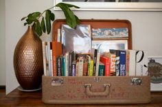 an old suitcase with books in it sitting on a table next to a vase and potted plant