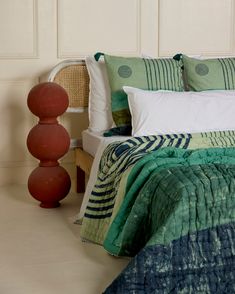 a bed with green and blue comforter next to two red vases